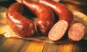 Domaća kobasica jeger narezana na drvenoj podlozi – suhomesnati proizvod bogatog okusa, idealan za sendviče i plate.