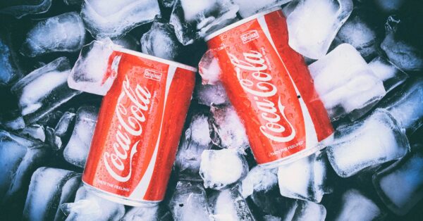 Dvije limenke Coca-Cole ohlađene u ledu, zorno prikazane s kapljicama kondenzacije na površini.