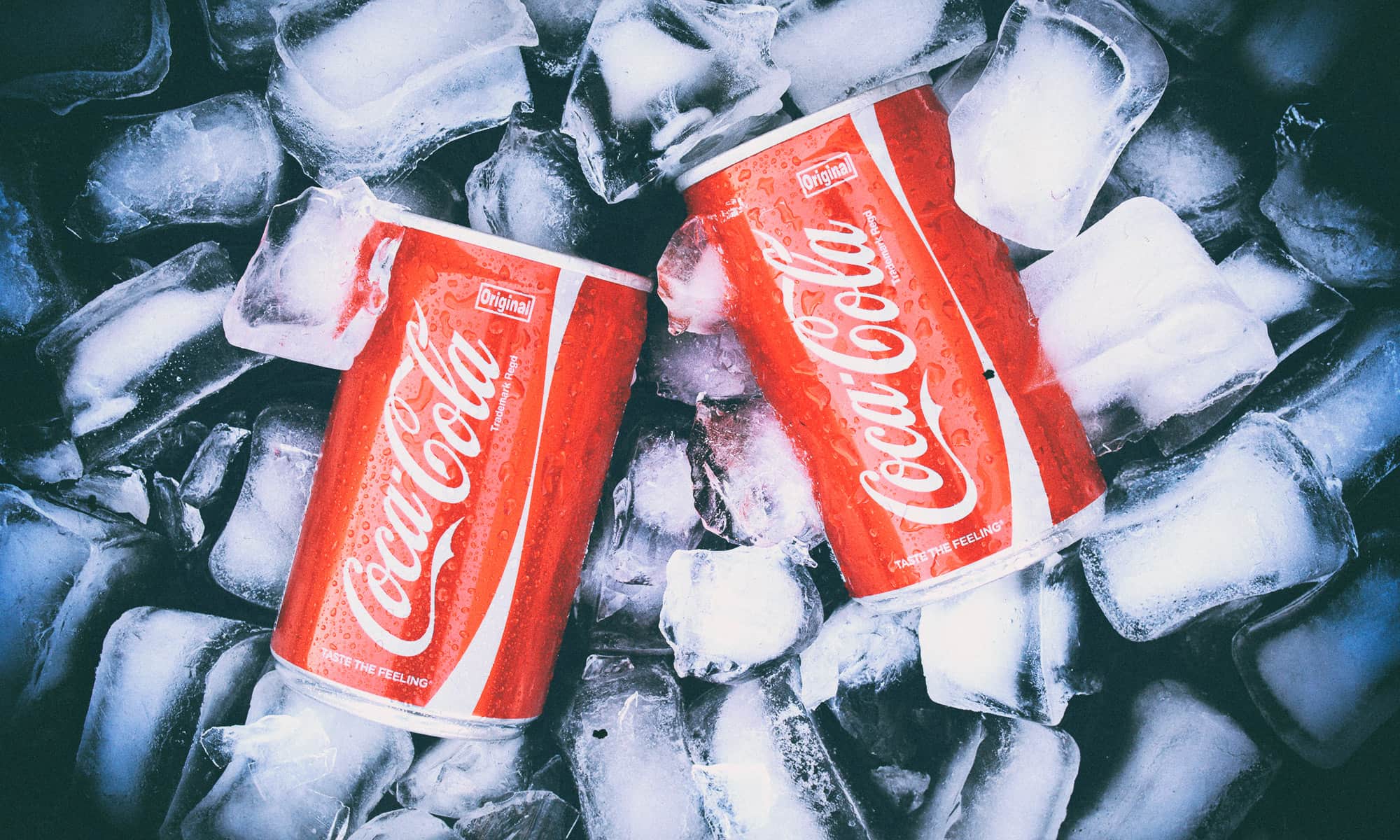 Dvije limenke Coca-Cole ohlađene u ledu, zorno prikazane s kapljicama kondenzacije na površini.