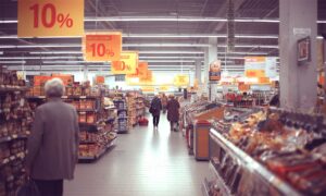 Starije osobe kupuju u supermarketu tijekom akcije s 10% popusta, u prolazu između polica punih prehrambenih proizvoda.